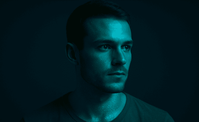 A ilusão da memória: Retrato de um homem com expressão pensativa, iluminado por uma luz azul-esverdeada em um ambiente escuro, sugerindo introspecção, mistério e a complexidade da mente humana.